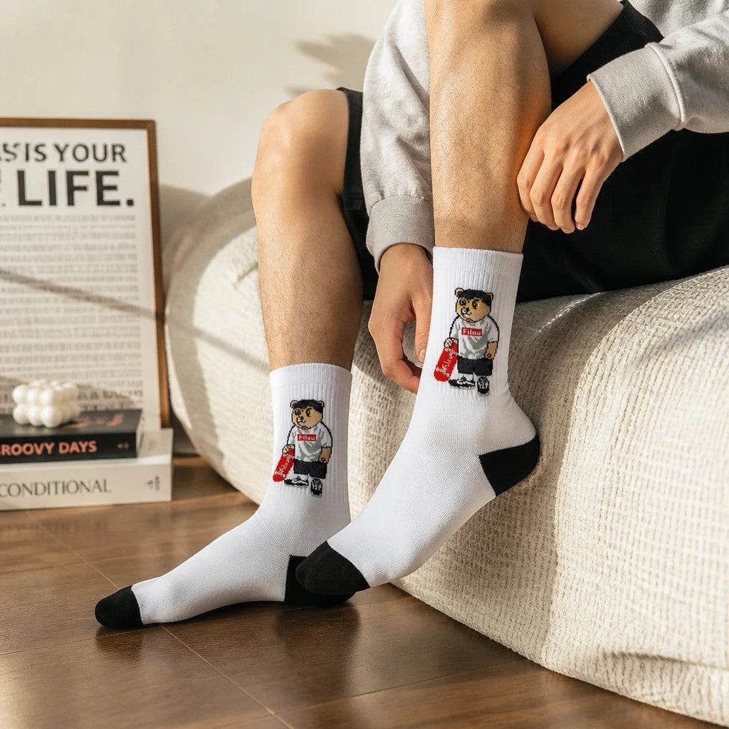 Qorapa LaraLara white crew socks featuring a bear with a skateboard graphic, black toe and heel, worn by a person.