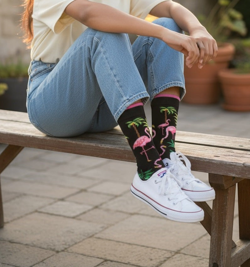 Qorapa LaraLara black crew socks featuring a pink flamingo and palm tree pattern worn with white sneakers