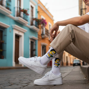 Qorapa LaraLara white crew socks with Bart Simpson graphic worn by a person in white sneakers on a colorful street.