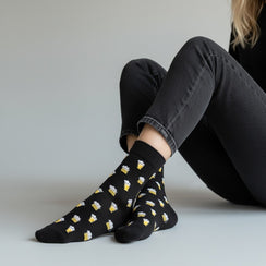 Qorapa LaraLara black crew socks featuring a repeating beer mug pattern worn by a person in grey jeans