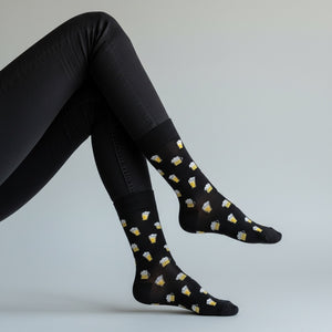 Qorapa LaraLara black crew socks with a repeating yellow and white beer mug pattern worn on a model