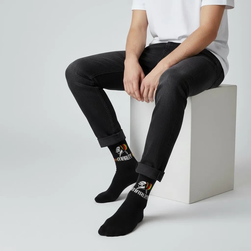Qorapa LaraLara black crew socks featuring a Bob Marley graphic print with Rasta-inspired accents on a seated model