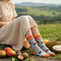 Qorapa LaraLara light blue crew socks with coconut print and orange accents worn by a woman in a sunny outdoor field.