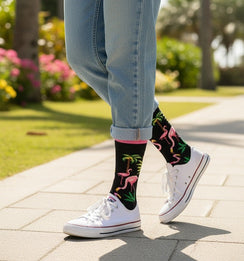 Qorapa LaraLara black crew socks featuring a pink flamingo and palm tree tropical design worn with white sneakers