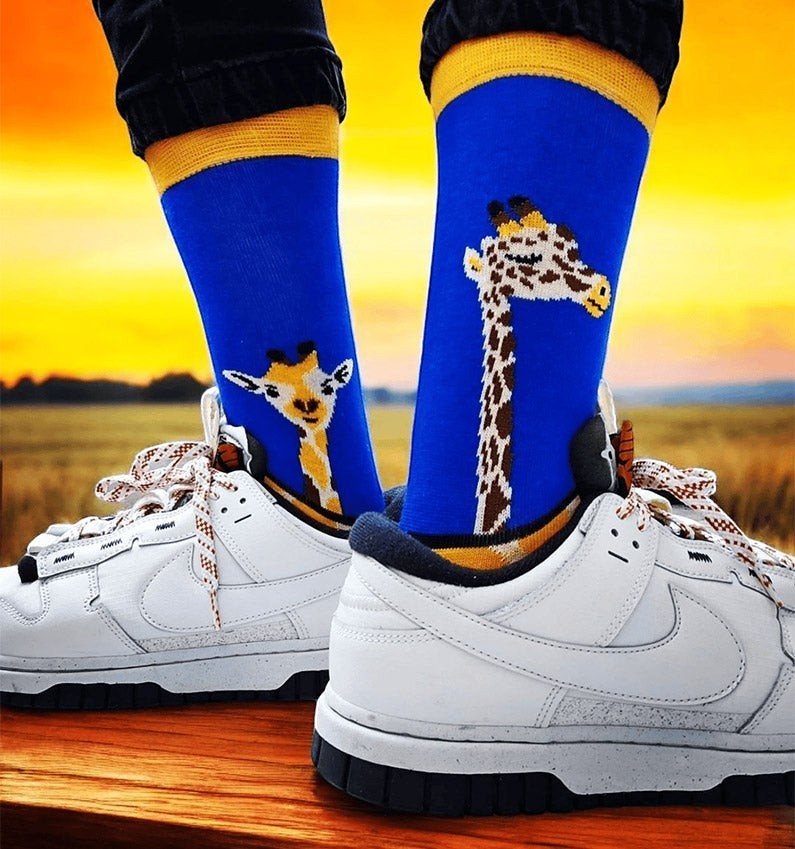 Qorapa LaraLara royal blue crew socks with giraffe pattern and yellow cuffs worn with white sneakers at sunset