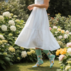 Qorapa LaraLara sage green cotton crew socks with white daisy floral pattern worn by a woman in a white dress in a garden