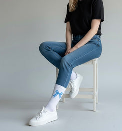 Qorapa LaraLara white crew socks with a blue bow print worn by a person in jeans and white sneakers