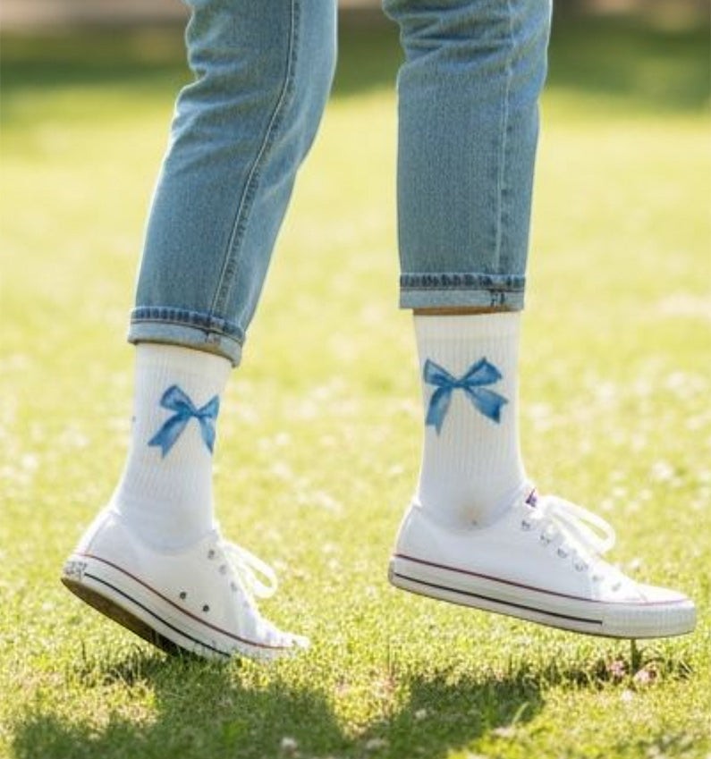 Qorapa LaraLara white crew socks with blue bow print worn with blue jeans and white sneakers on a grassy lawn