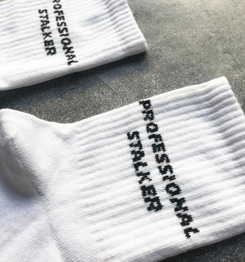 Qorapa LaraLara white cotton-blend crew socks featuring black embroidered PROFESSIONAL STALKER text on the ribbed cuff.
