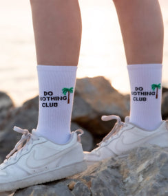 Qorapa LaraLara white crew socks featuring a Do Nothing Club graphic and palm tree motif worn with white sneakers