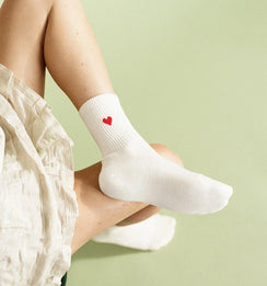 Qorapa LaraLara white cotton crew socks with a small embroidered red heart on the ribbed cuff worn by a person