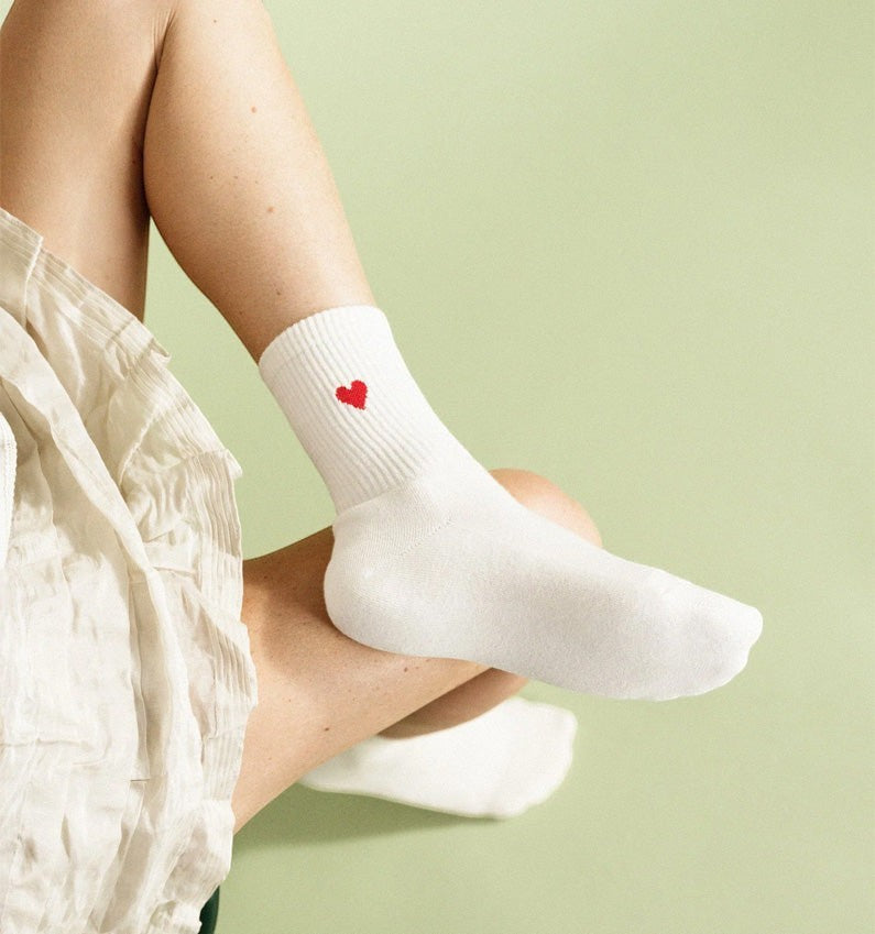 Qorapa LaraLara white cotton crew socks with a small embroidered red heart on the ribbed cuff worn by a person