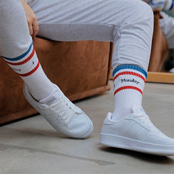 Qorapa LaraLara white low-top athletic sneakers worn with striped crew socks, featuring a minimalist court design.