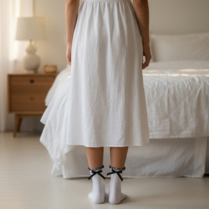 Qorapa LaraLara white ankle socks with ruffled cuffs and black ribbon bows worn with a white skirt in a bedroom